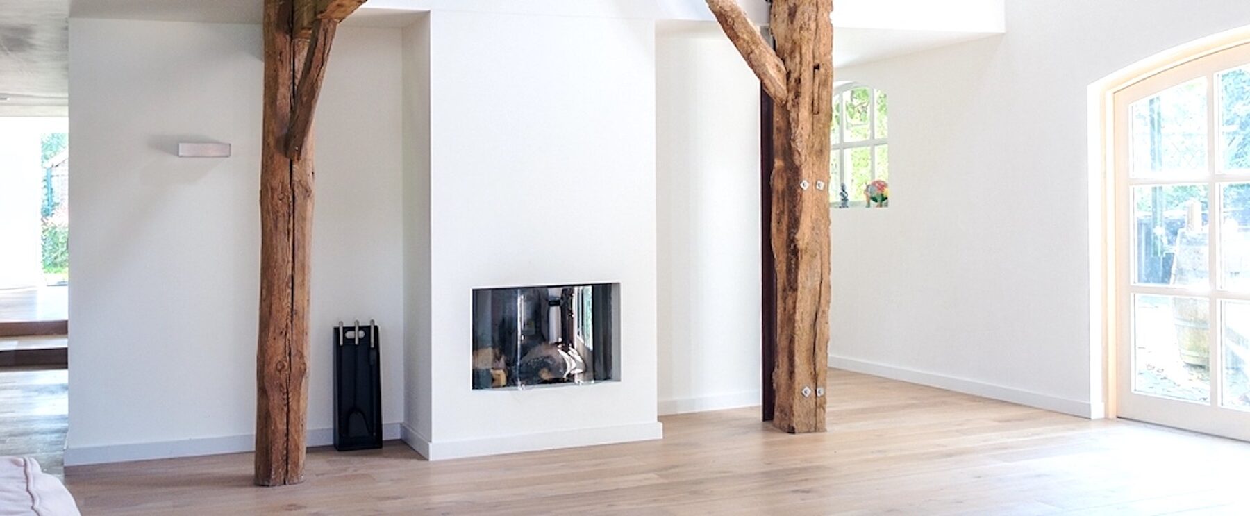 Glad gestuukte witte wanden met houten spanten en een inbouwhaard